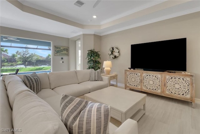 living area featuring a tray ceiling, crown molding, visible vents, a ceiling fan, and baseboards