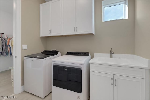 laundry area featuring washer and clothes dryer, a sink, cabinet space, and light wood-style floors