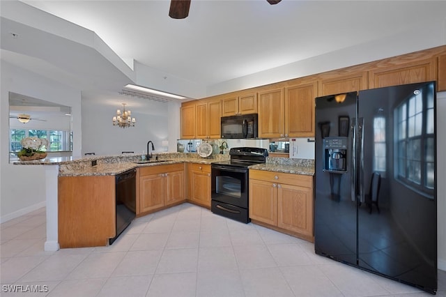 kitchen with a peninsula, light stone countertops, black appliances, a sink, and ceiling fan with notable chandelier