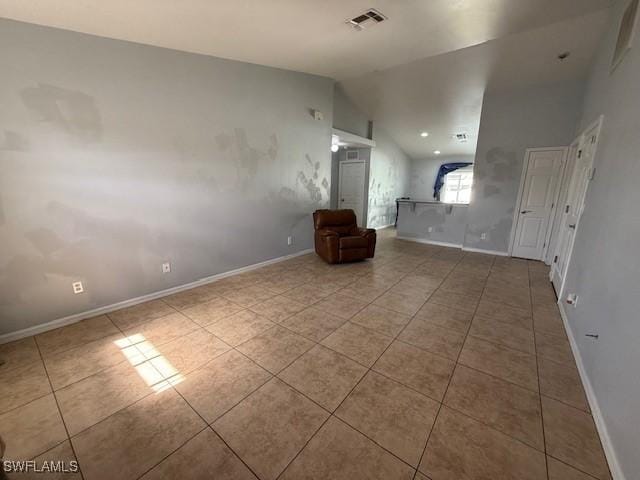 empty room with lofted ceiling, light tile patterned floors, baseboards, and visible vents