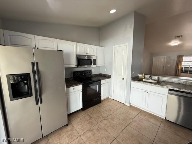 kitchen with light tile patterned floors, stainless steel appliances, white cabinets, vaulted ceiling, and a sink