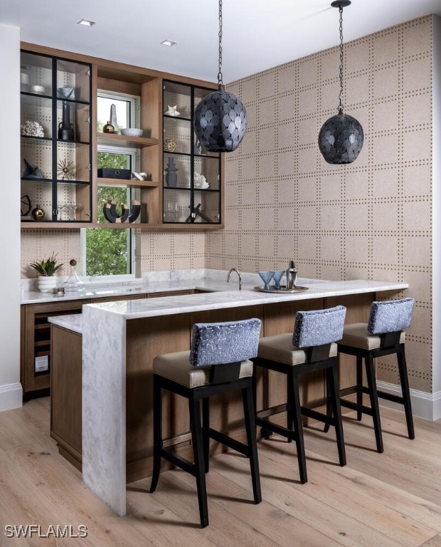 bar featuring baseboards, hanging light fixtures, and light wood-style floors