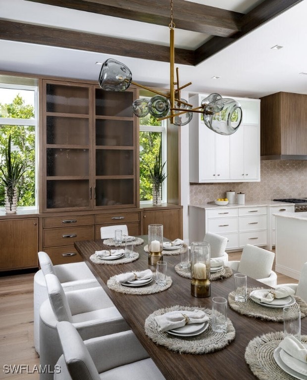 dining area featuring a chandelier, a wealth of natural light, beamed ceiling, and light wood-style flooring