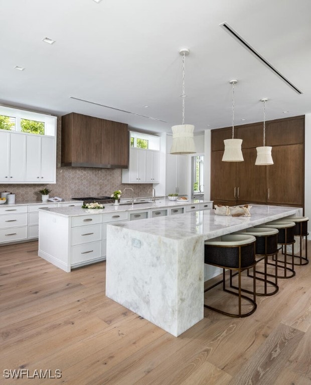 kitchen with a spacious island, light wood-type flooring, backsplash, and white cabinets