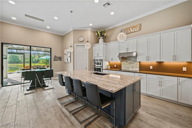 kitchen with pendant lighting, white cabinetry, visible vents, and under cabinet range hood