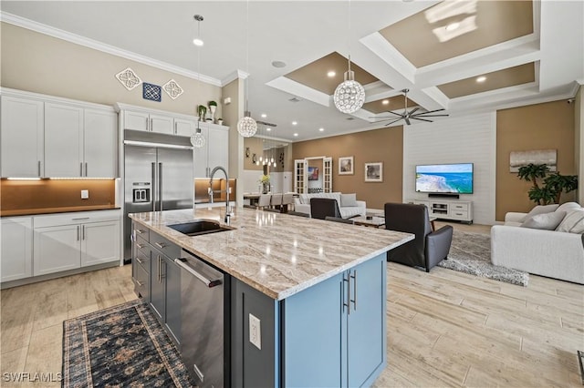 kitchen with stainless steel appliances, a sink, white cabinets, open floor plan, and a center island with sink