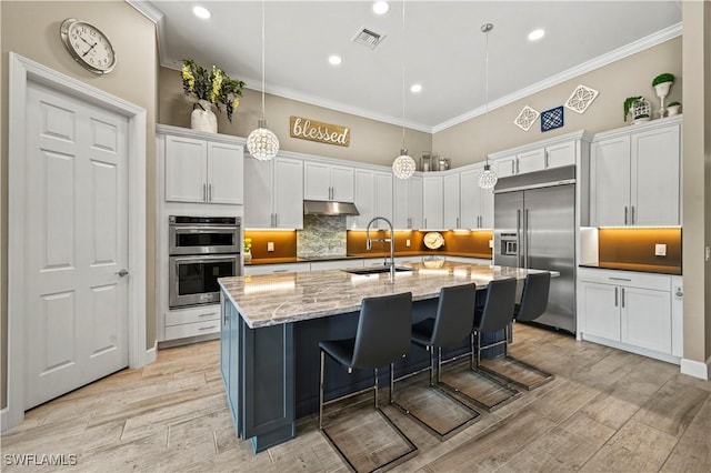 kitchen featuring appliances with stainless steel finishes, an island with sink, decorative light fixtures, and white cabinets