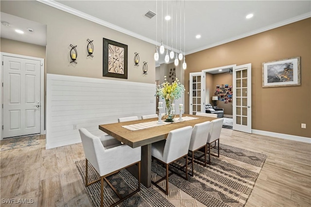 dining area with light wood-style flooring, a wainscoted wall, visible vents, french doors, and crown molding