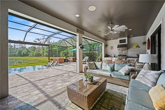 view of patio with ceiling fan, an outdoor kitchen, a lanai, outdoor lounge area, and a water view