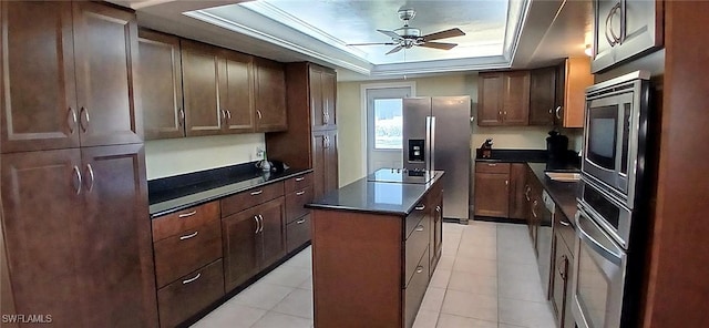 kitchen featuring a tray ceiling, a center island, dark countertops, appliances with stainless steel finishes, and ceiling fan