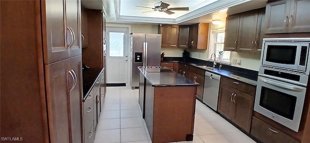 kitchen featuring a raised ceiling, dark countertops, a kitchen island, stainless steel appliances, and a sink