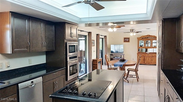 kitchen featuring light tile patterned floors, ornamental molding, appliances with stainless steel finishes, dark stone counters, and a raised ceiling