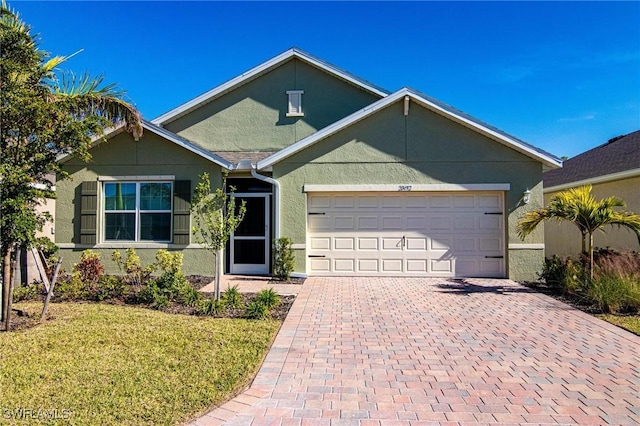 ranch-style home featuring a front lawn, decorative driveway, an attached garage, and stucco siding