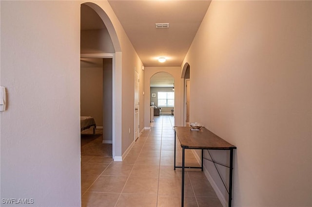 corridor featuring light tile patterned floors, baseboards, visible vents, and arched walkways