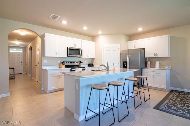 kitchen with light countertops, appliances with stainless steel finishes, an island with sink, and white cabinetry