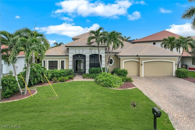 mediterranean / spanish house with an attached garage, a tile roof, decorative driveway, stucco siding, and a front lawn