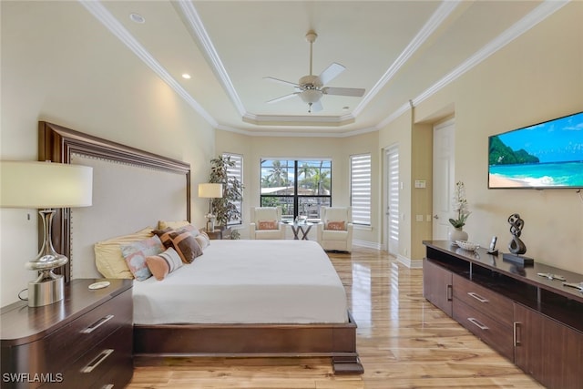 bedroom featuring ornamental molding, a tray ceiling, baseboards, and light wood finished floors