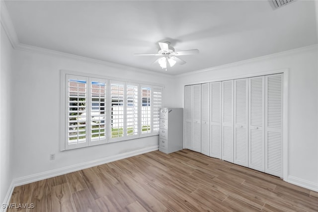 unfurnished bedroom featuring ceiling fan, baseboards, light wood-style floors, ornamental molding, and a closet