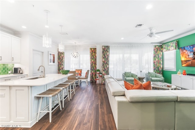 living area featuring visible vents, ornamental molding, dark wood-type flooring, ceiling fan with notable chandelier, and recessed lighting