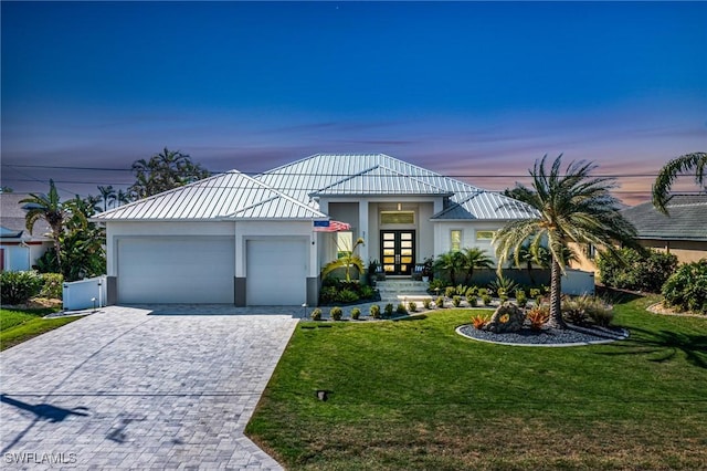 view of front of home with metal roof, a garage, a yard, decorative driveway, and stucco siding