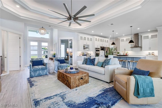 living room with recessed lighting, a ceiling fan, french doors, light wood-type flooring, and a tray ceiling