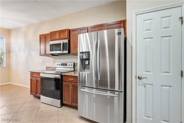 kitchen featuring light tile patterned floors, stainless steel appliances, brown cabinetry, light stone countertops, and baseboards