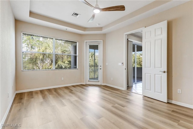 empty room featuring light wood-style floors, visible vents, a tray ceiling, and baseboards