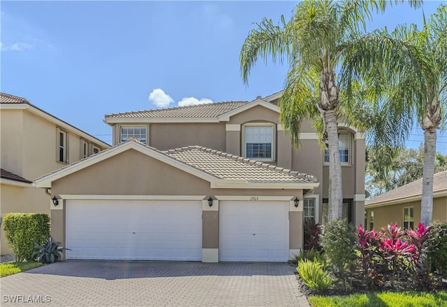 view of front facade featuring a garage, a tile roof, decorative driveway, and stucco siding