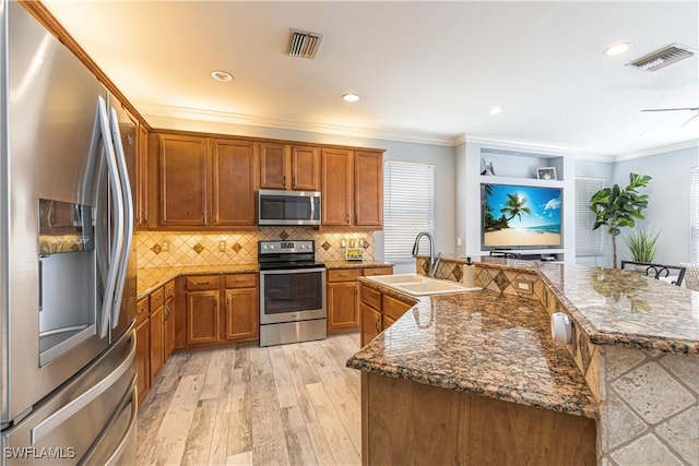 kitchen with stainless steel appliances, brown cabinetry, a sink, and visible vents