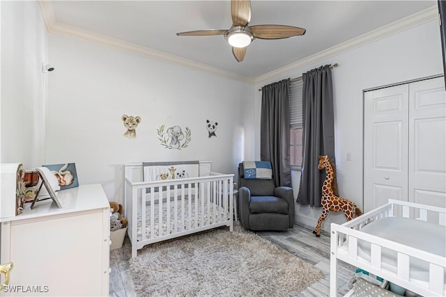 bedroom with ceiling fan, wood finished floors, ornamental molding, a closet, and a crib