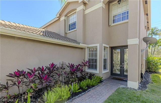 view of exterior entry featuring stucco siding, a tiled roof, and french doors