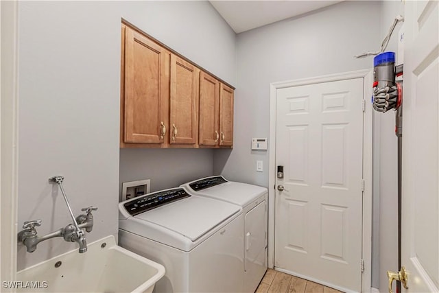 clothes washing area with a sink, light wood-type flooring, washing machine and dryer, and cabinet space