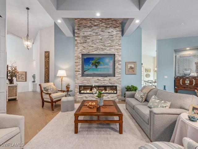 living area with light wood-type flooring, an inviting chandelier, recessed lighting, and a stone fireplace