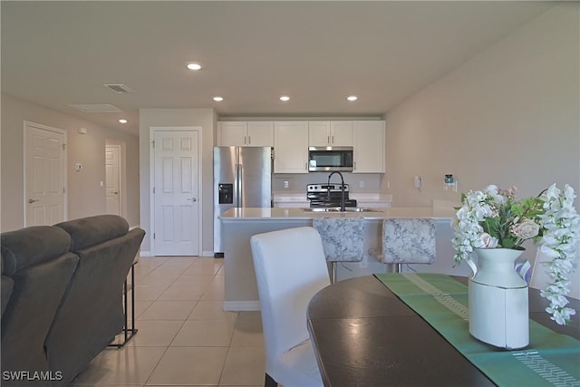 kitchen with light tile patterned floors, stainless steel appliances, a sink, white cabinets, and light countertops