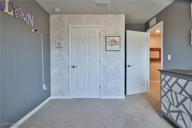 unfurnished bedroom with light colored carpet, a walk in closet, visible vents, and baseboards