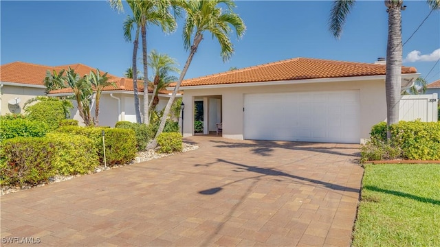 view of front of house with decorative driveway, an attached garage, a tile roof, and stucco siding