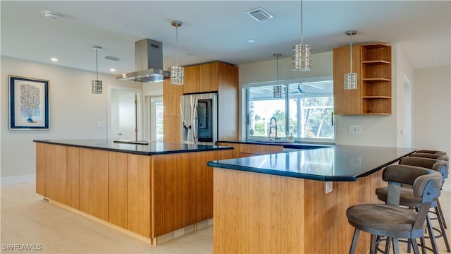 kitchen with island exhaust hood, stainless steel refrigerator with ice dispenser, dark countertops, visible vents, and a sink