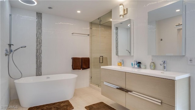 full bathroom featuring tile walls, double vanity, a freestanding bath, a stall shower, and a sink