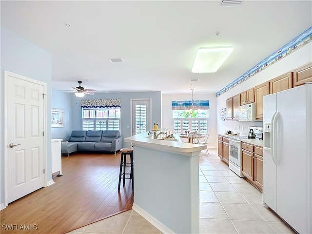 kitchen with white appliances, a kitchen breakfast bar, open floor plan, light countertops, and a center island with sink