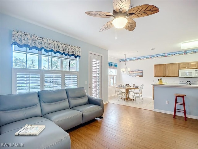 living room featuring light wood-style floors, visible vents, baseboards, and ceiling fan with notable chandelier