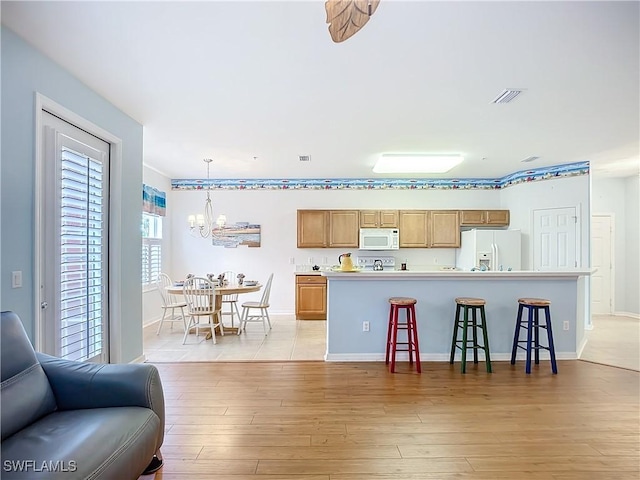 kitchen featuring white appliances, visible vents, hanging light fixtures, light countertops, and light wood-type flooring