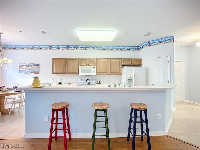 kitchen with white appliances, a kitchen island, visible vents, a kitchen breakfast bar, and light countertops