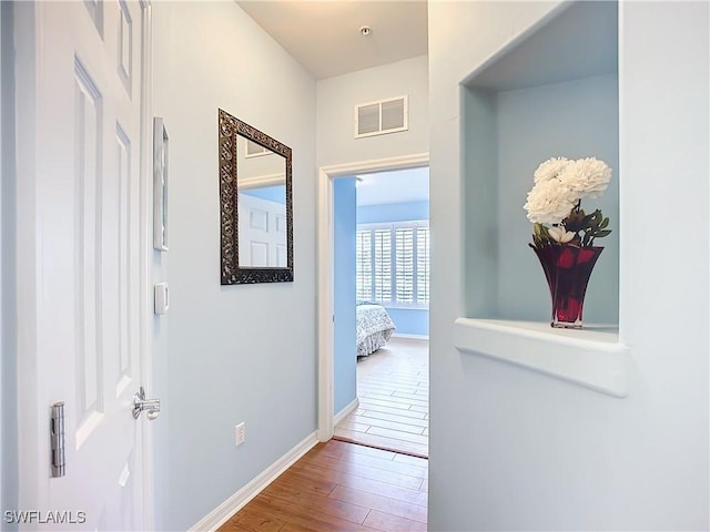 hallway with visible vents, baseboards, and wood finished floors