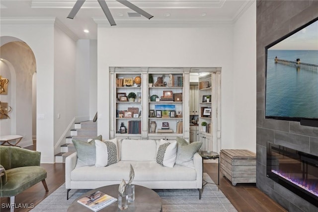 living area with arched walkways, ornamental molding, and wood finished floors