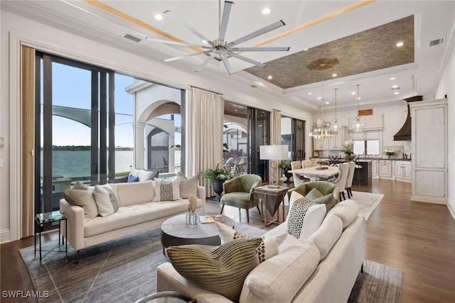 living room with visible vents, dark wood-style floors, ornamental molding, a water view, and a tray ceiling