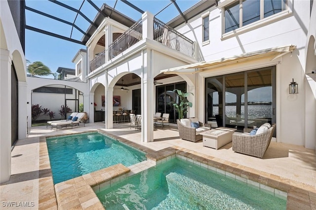 rear view of house featuring stucco siding, a ceiling fan, glass enclosure, a balcony, and an outdoor living space