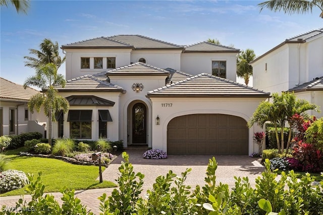 mediterranean / spanish house featuring a tiled roof, an attached garage, decorative driveway, a front lawn, and stucco siding