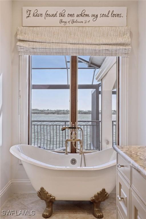 bathroom featuring a water view, baseboards, a freestanding bath, and vanity