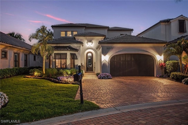 view of front of home featuring an attached garage, decorative driveway, a front yard, and stucco siding