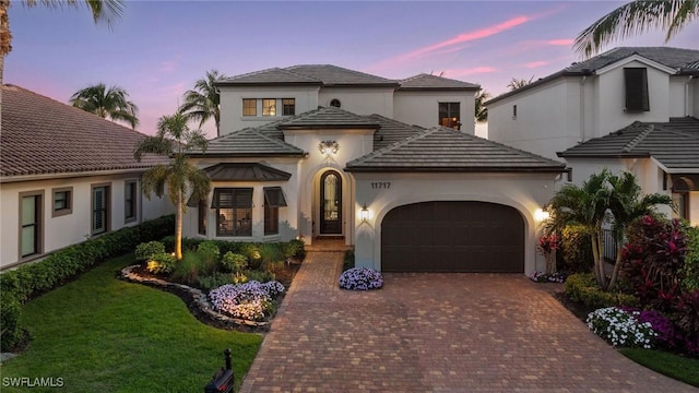 mediterranean / spanish home featuring a garage, decorative driveway, a lawn, and stucco siding